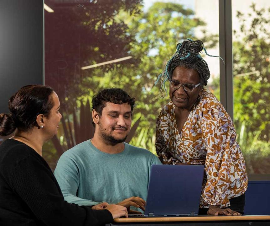Students and a teacher look at a laptop