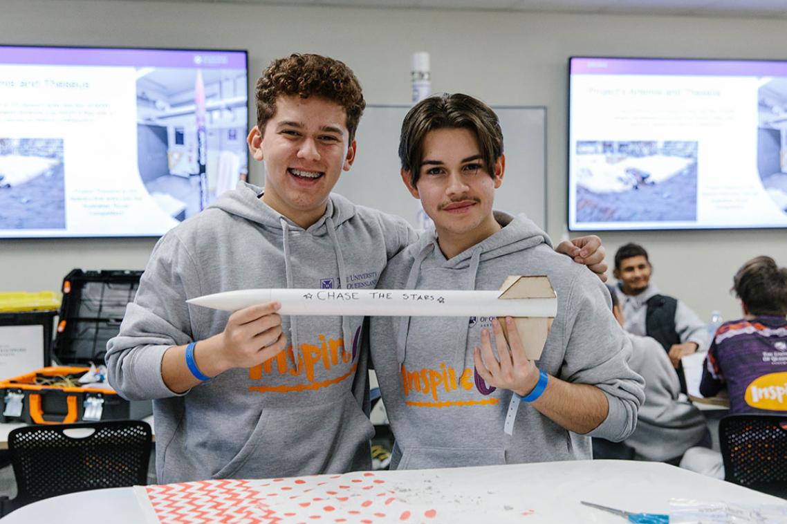 Two InspireU students holding a small cardboard rocket that says 'Chase the stars'